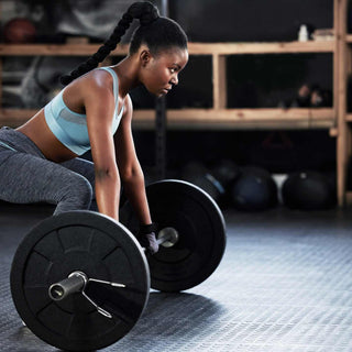 A woman standing crouched, her hands on a loaded barbell