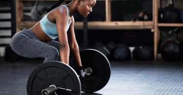 A woman standing crouched, her hands on a loaded barbell